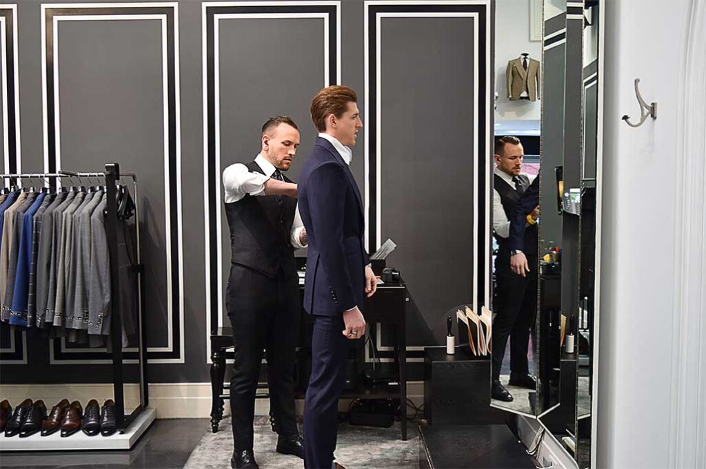 Tailor adjusting a man's suit in a fitting room at Michael Andrews Bespoke, showcasing the custom tailoring process