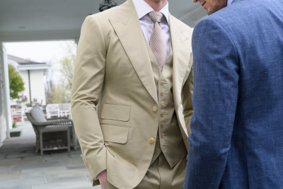 Tan three-piece custom suit with notch lapel, matching waistcoat and tie, styled with a light dress shirt in an outdoor setting, paired with a blue suit, Kentucky Derby style guide.