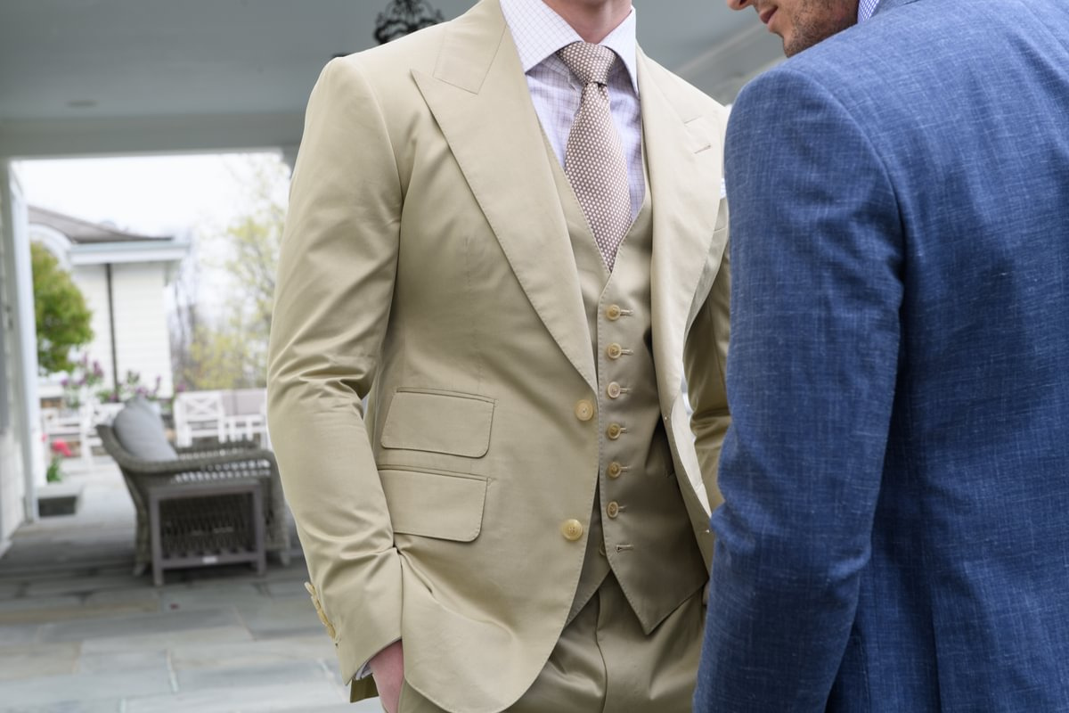 Tan three-piece custom suit with notch lapel, matching waistcoat and tie, styled with a light dress shirt in an outdoor setting, paired with a blue suit, Kentucky Derby style guide.