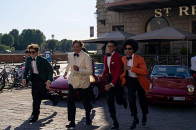 Four guests in colorful black tie run past vintage red cars outside The St. Regis Florence during Michael Andrews Bespoke’s 20th-anniversary Pitti Uomo celebration with Dormeuil.