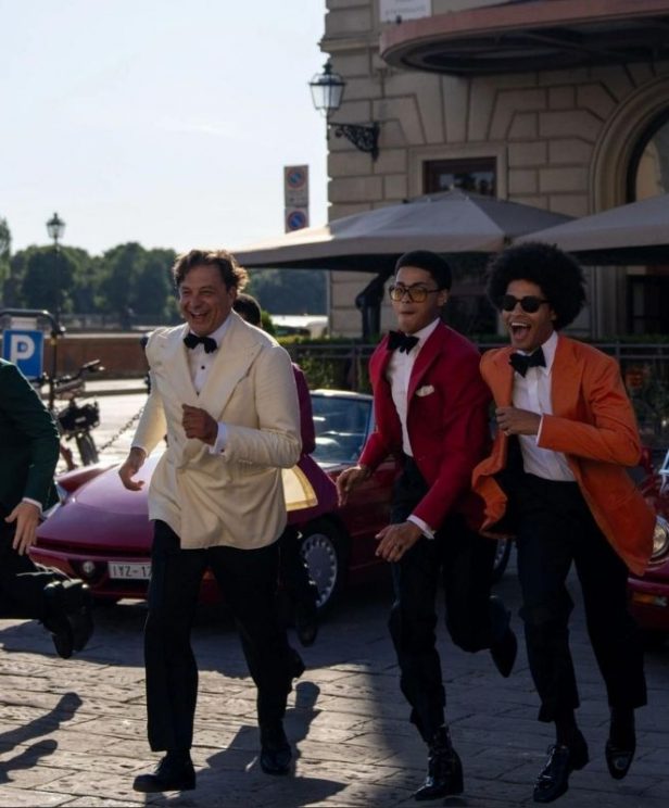 Four guests in colorful black tie run past vintage red cars outside The St. Regis Florence during Michael Andrews Bespoke’s 20th-anniversary Pitti Uomo celebration with Dormeuil.